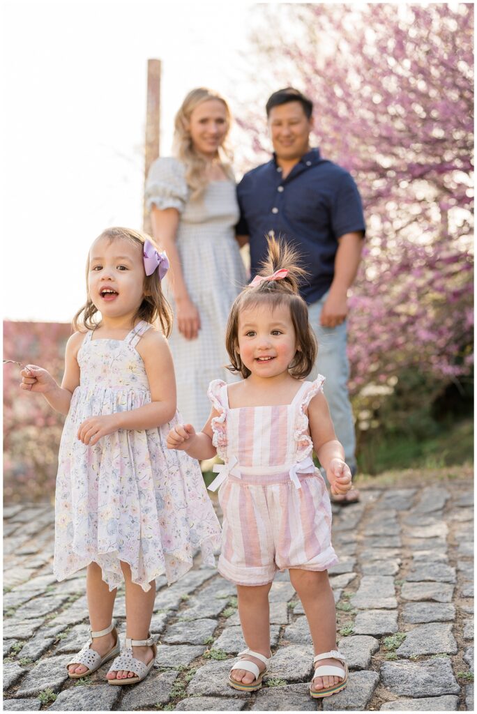 Two little girls stand with their spring outfits for their family session at Libby Hill as Mom and Dad stand in the background behind them!