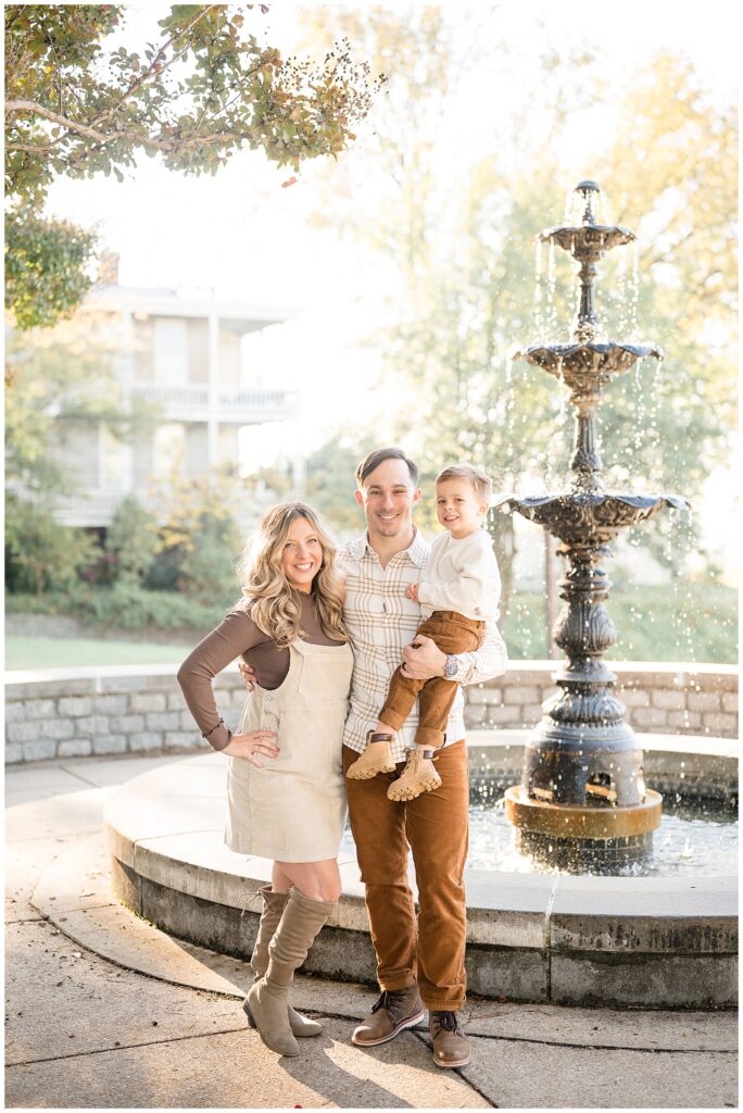 Mom and Dad stand by water fountain at Libby Hill Park in Richmond, VA with their son during their family photography session in the fall.