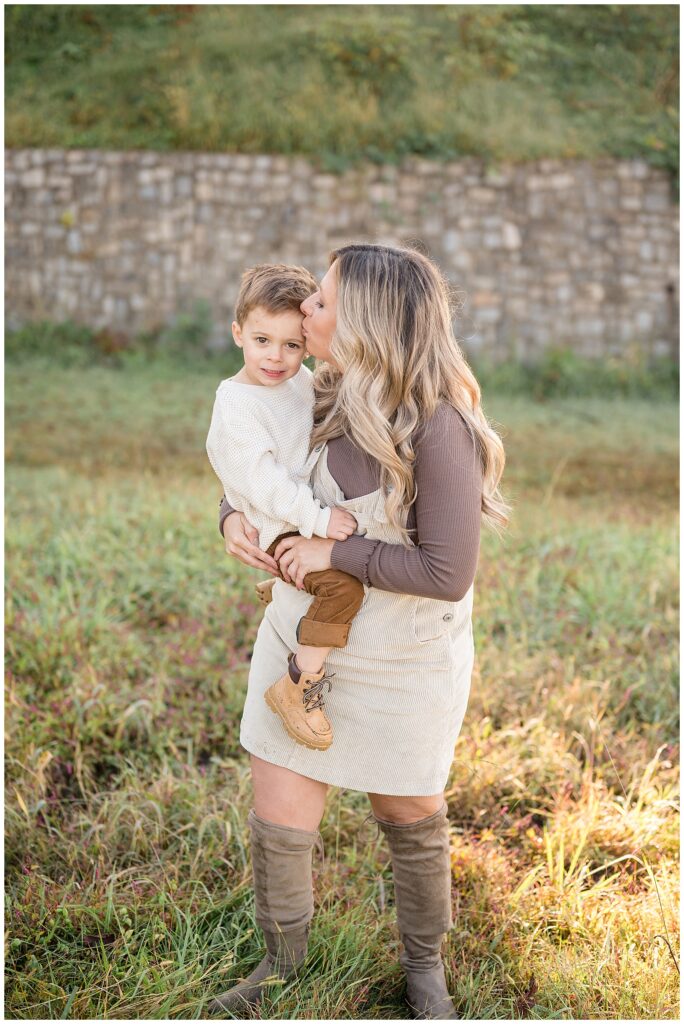 Mom holds son on hip as she kisses his forehead during their fall family session with Richmond, Virginia family photographer, Wisp + Willow Photography Co.