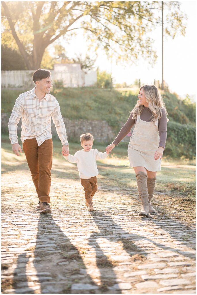 Mom and Dad hold hands of son in the middle of them as they walk along the cobblestone path of Libby Hill during their fall family session.