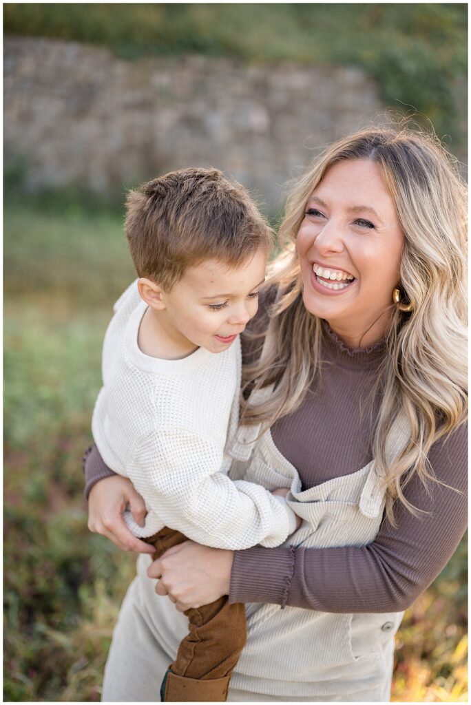 Mom holds boy on hip as they laugh and have fun together during their family session with Wisp + Willow Photography Co. in Richmond, VA at Libby Hill Park.