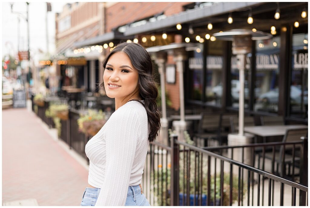 Senior Session in Downtown Square in McKinney, TX with girl wearing a white crop top and jeans, smiles at the camera.