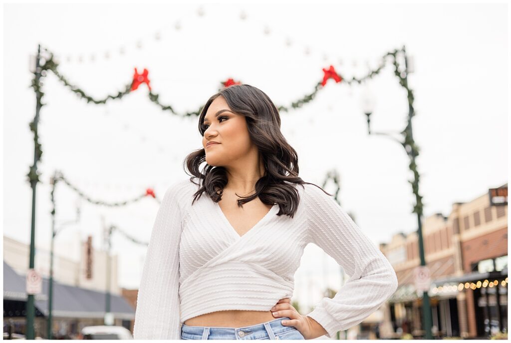 Senior session captured in Downtown McKinney, TX as girl stands in front of garland and red bows during the holidays.