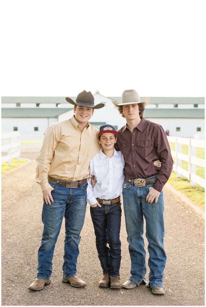 3 brothers stand in front of the Harlinsdale Farm barn in Franklin, TN wearing cowboy boots and hats.