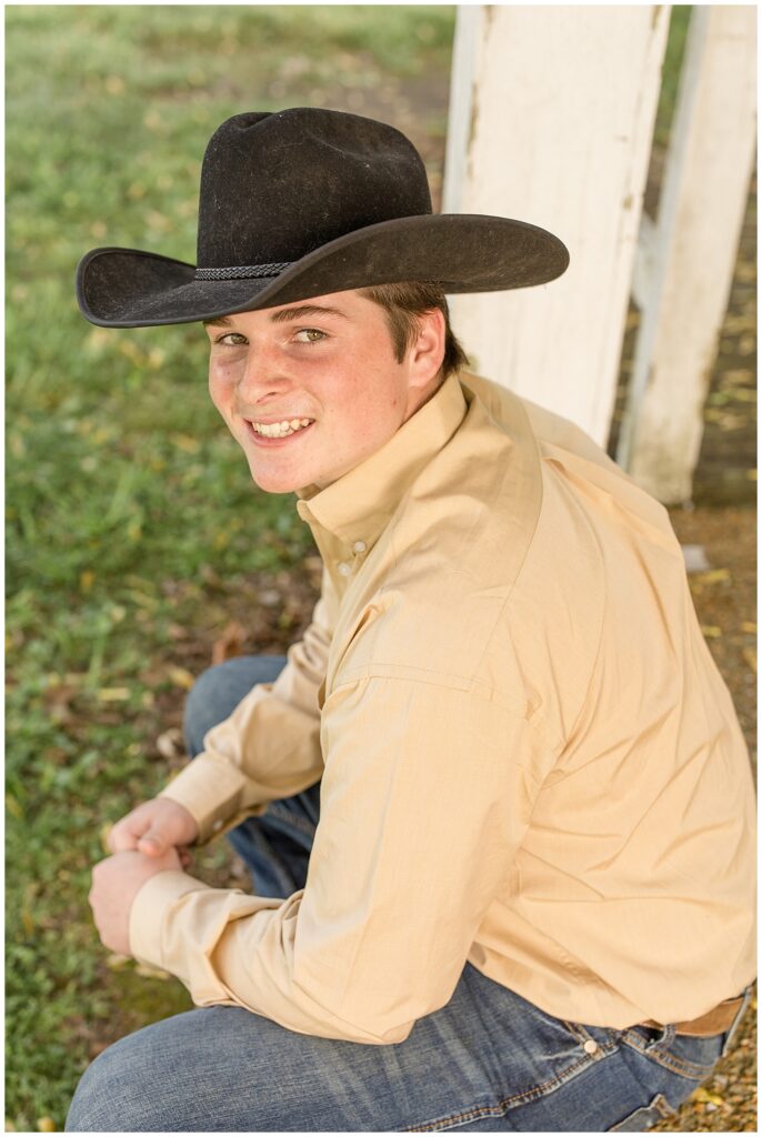 Teen boy wears a black cowboy hat and tan button up shirt and jeans as he sits on the farm steps at Halinsdale Farm in Franklin, TN.