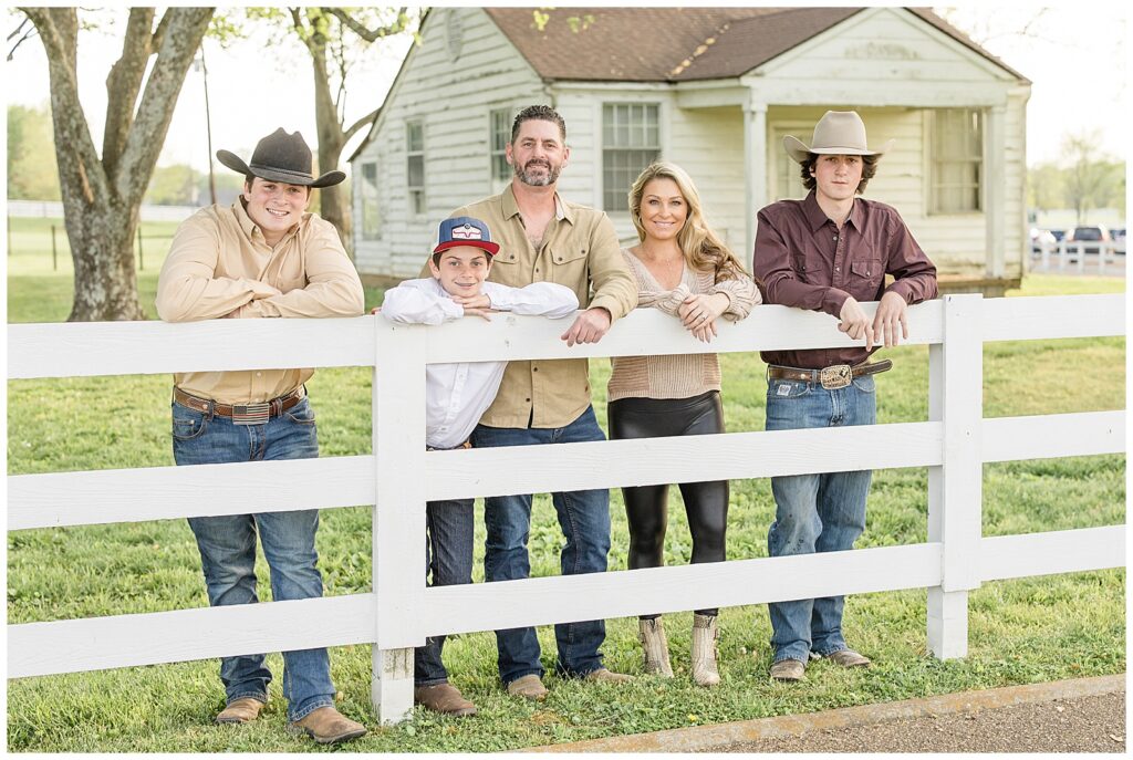 Franklin family photographer, Wisp + Willow Photography Co. stand behind white fence during their family mini-session with Wisp + Willow Photography Co.  Family wears neutrals colors, cowboy boots, and hats!