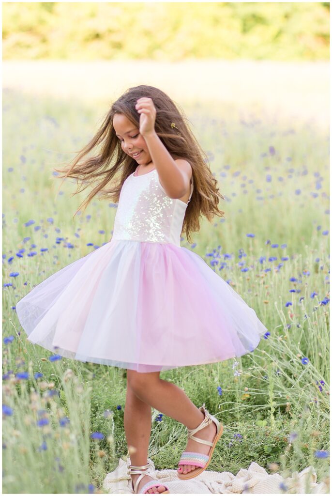 Little girl wears sparkly dress and purple tulle skirt as she twirls in field of flowers.  Texas family photographer, Wisp + Willow Photography Co. capture the perfect moment.