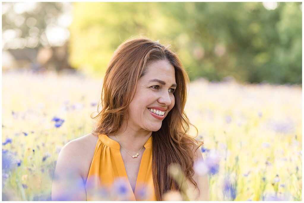 Woman takes new headshots during wildflower mini session wearing a bright yellow/orange v-neck dress as she smiles off in the distance.  