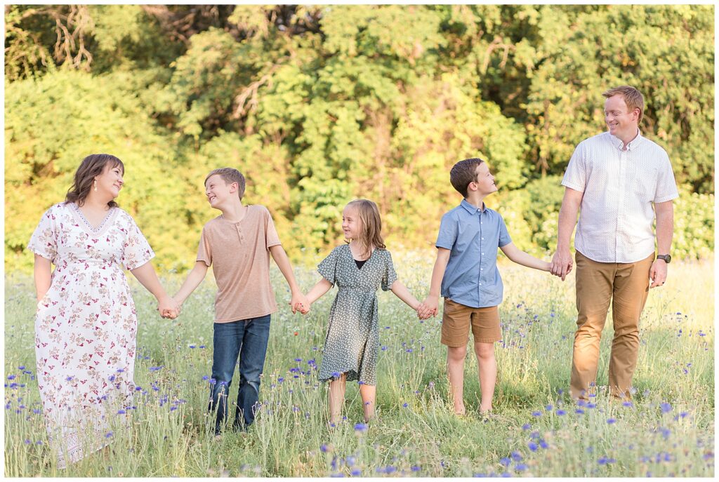 Family of 5 hold hands in straight line and look and smile at each other during their family photography mini session in Richardson, TX.