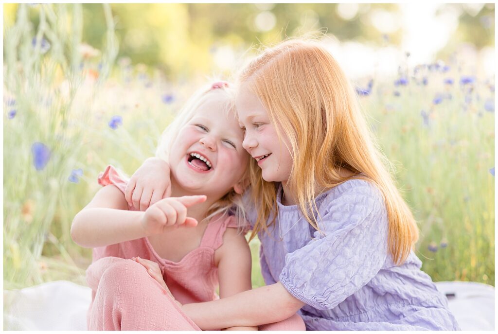Two sisters laugh at something funny as older red head sisters hugs little sister and points at something past the camera. Texas family photographer, Wisp + Willow Photography Co. capture a great sister moment.