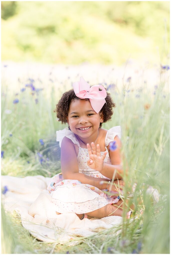 Little girl holds up 4 fingers in wildflower field to show she is 4 years old.  Texas family photographer, Wisp + Willow Photography Co. capture a milestone for this little girl.