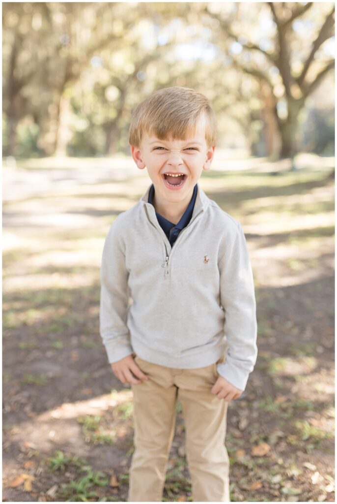 Little boy smiles big for savannah family photographer, Wisp + Willow Photography Co., wearing a blue collared shirt with a cream zip up sweater over it.