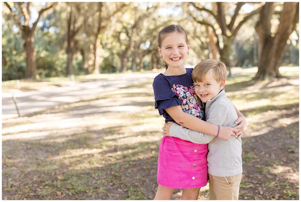 Brother and sister hug each other as they smily at the camera of Wisp + Willow Photography Co. during their fall mini session.