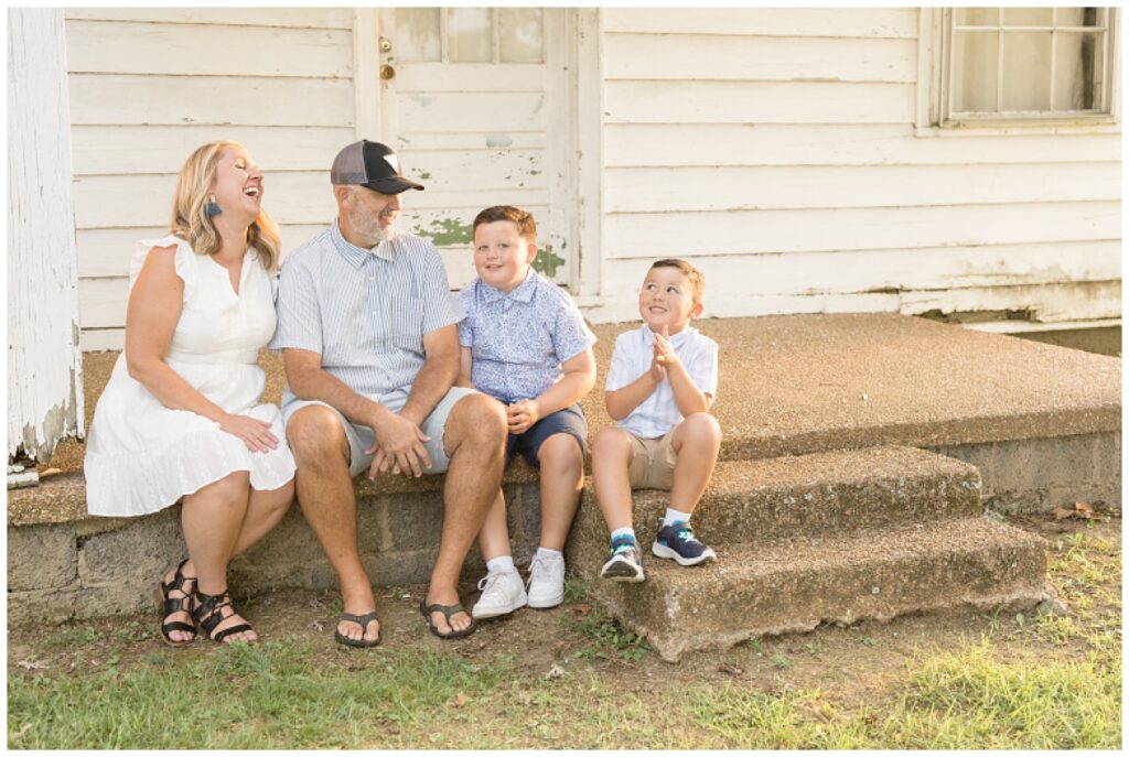 Mom and Dad laugh with their two boys during their Franklin family session as they sit on steps in front of old house.