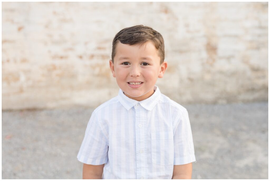 Little boy wears white and blue striped button up shirt as he smiles at the camera of Wisp + Willow Photography Co.