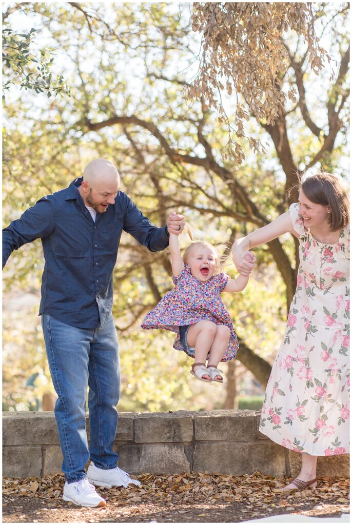 A joyful image of Mom and Dad holding the hands of toddler daughter  who jumps of small rock wall with such excitement.  Check out Wisp + Willow Photography Co. blog to see more now!