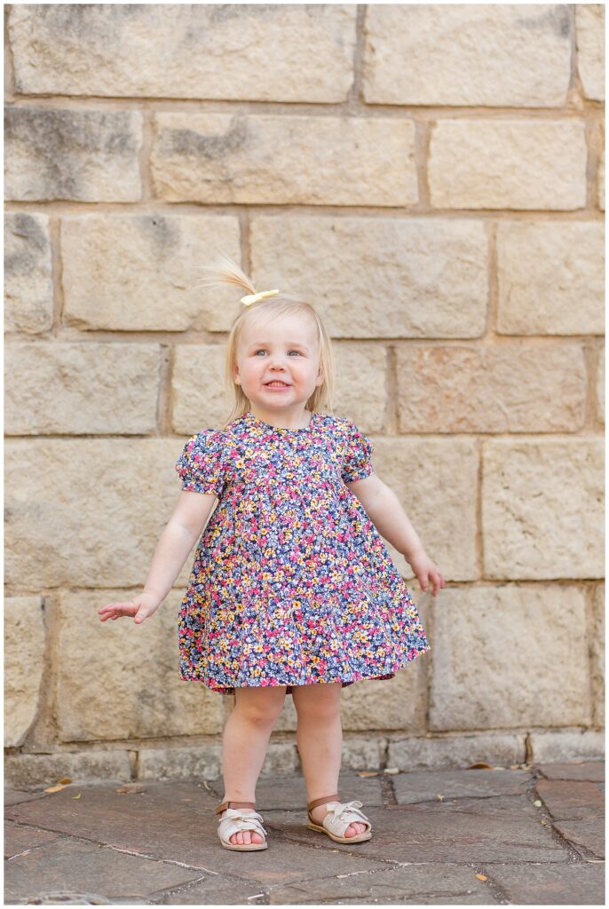 Toddler girl wears floral dress and yellow bow during her family portrait session with Frisco family photographer, Wisp + Willow Photography Co.