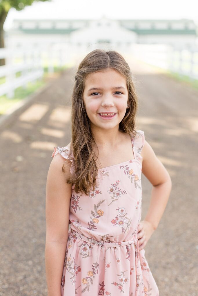 Little girl stands with her hand on her hip and the other on the side as she wears a light pink, floral dress for her sibling photography session with Wisp + Willow Photography Co. in Franklin, TN.