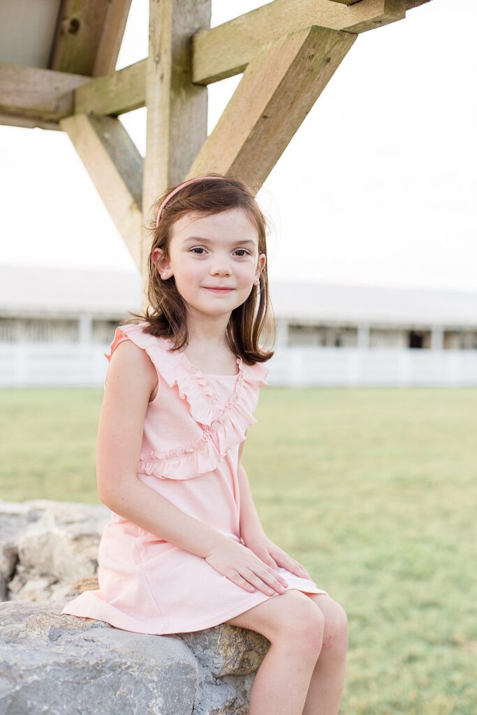 Little girl wears a light pink dress and a matching skinny headband as she looks at the camera of Wisp + Willow Photography Co. during her sibling photography session in Franklin, TN.