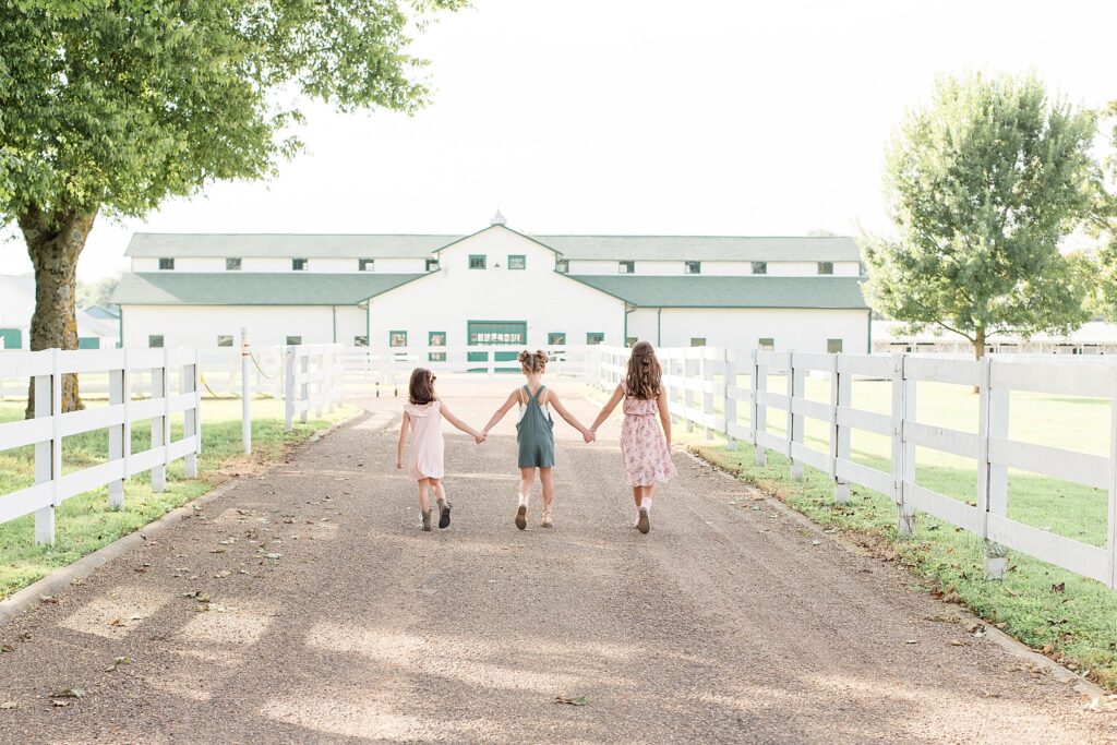 Three sisters walk away from the camera holding hands as they walk back towards Harlinsdale Farm in Franklin, TN.