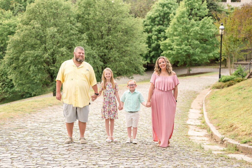 A mom, dad, and two kids - a boy and a girl, walk down the cobblestone path at Libby Hill in Richmond, VA during their family portrait session.