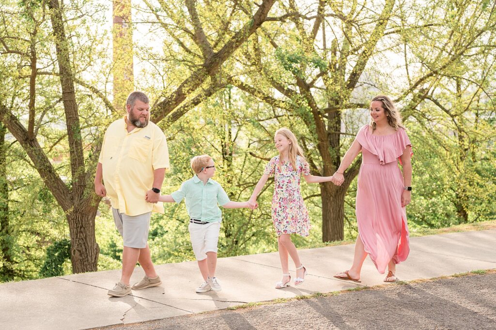 Family of 4 hold hands as they walk together in the following order, Dad, son, daughter, and Mom during their family session at Libby Hill Park in Richmond, VA.