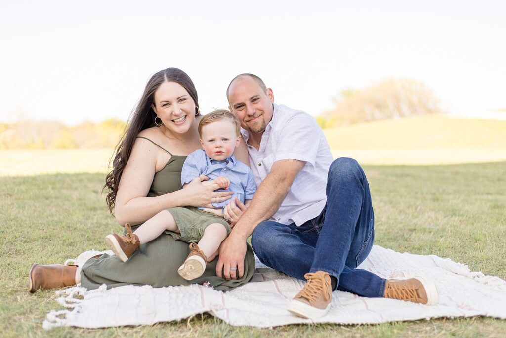 Family of 3 smile at camera with their toddler son during their family portrait session in McKinney, TX.
