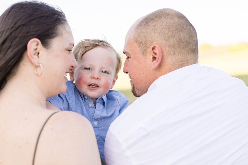 Wisp + Willow Photography Co. captures toddler boy smiling over parents shoulders as they look at each other.