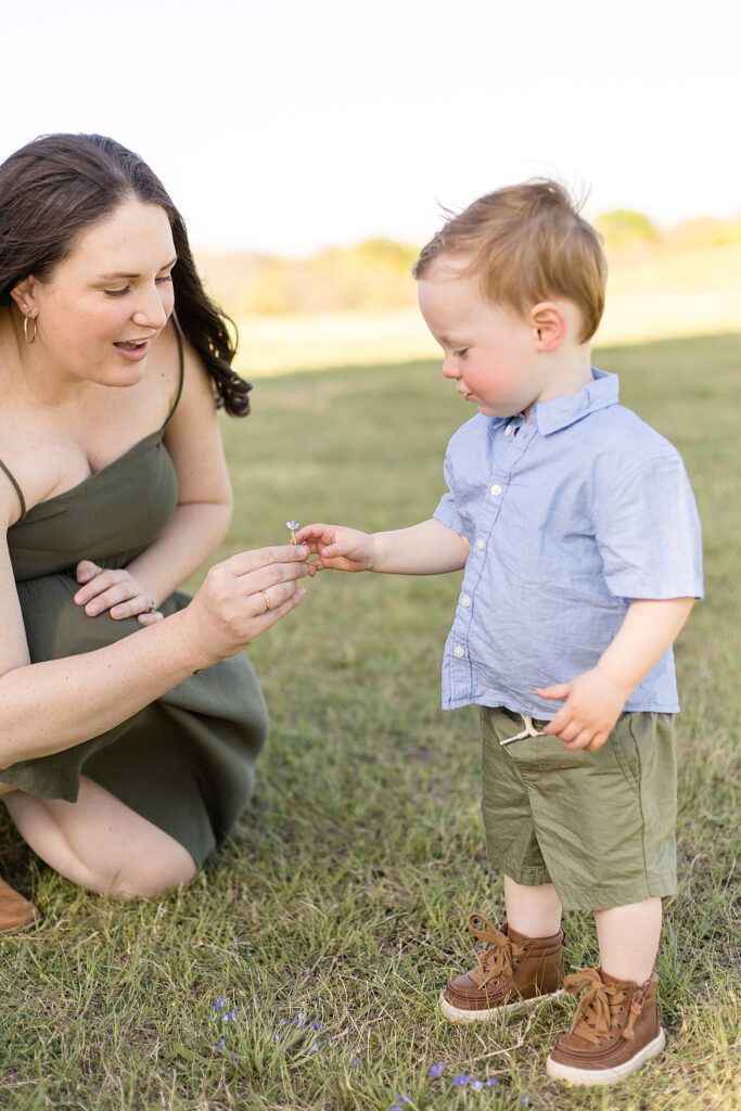 McKinney family photography captures mom giving toddler son a wildflower from the grass during their family portrait session.