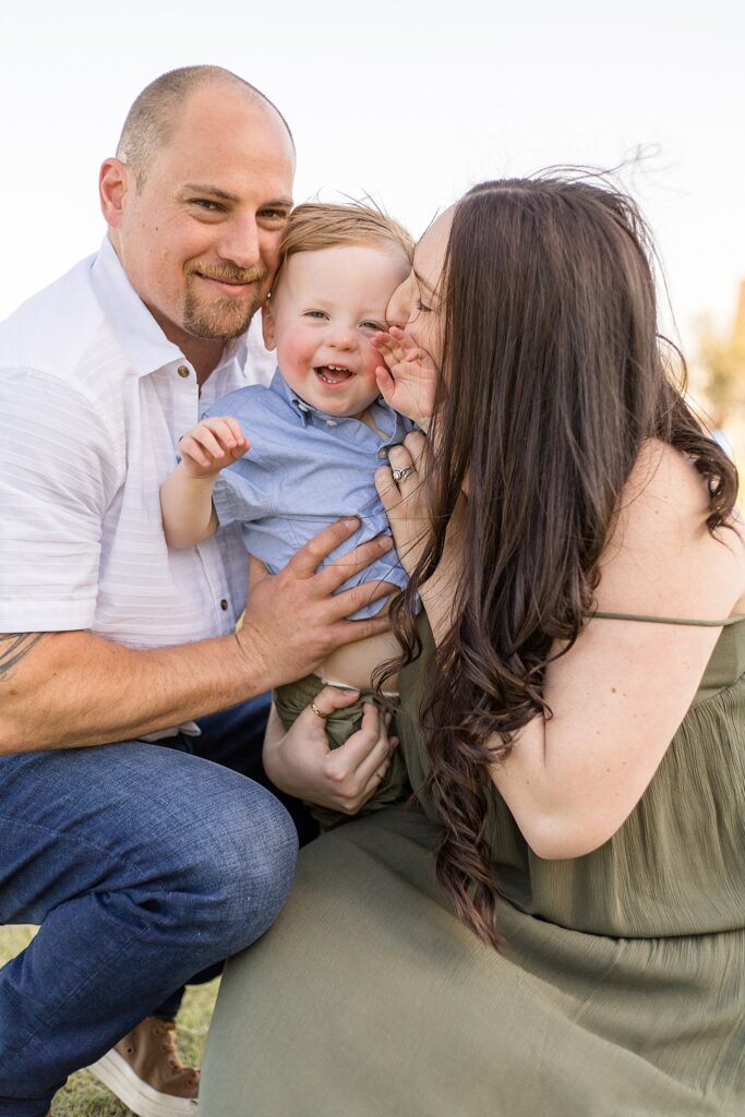 Mom gives toddler son a kiss on his cheek while Dad and son go cheek to cheek smiling at the camera during their family session with Wisp + Willow Photography Co.