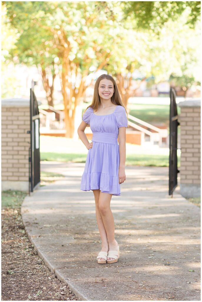 Plano Senior Session with senior wearing a purple dress and standing in front of open black gate.