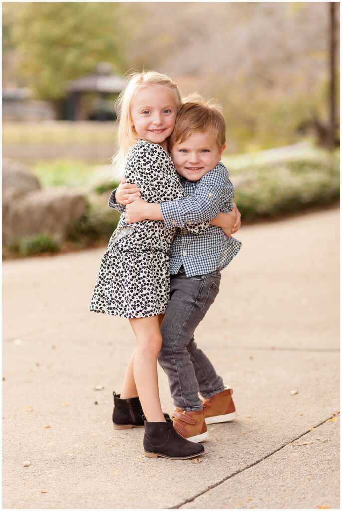 Older sister hugs toddler brother during their family photography session at Pullen Park in Raleigh, NC.