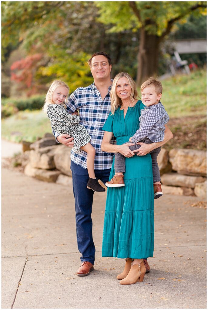 Mom and Dad each hold a child on their hip as they smile at the camera of Wisp + Willow Photography Co. during their family session in Raleigh, NC.