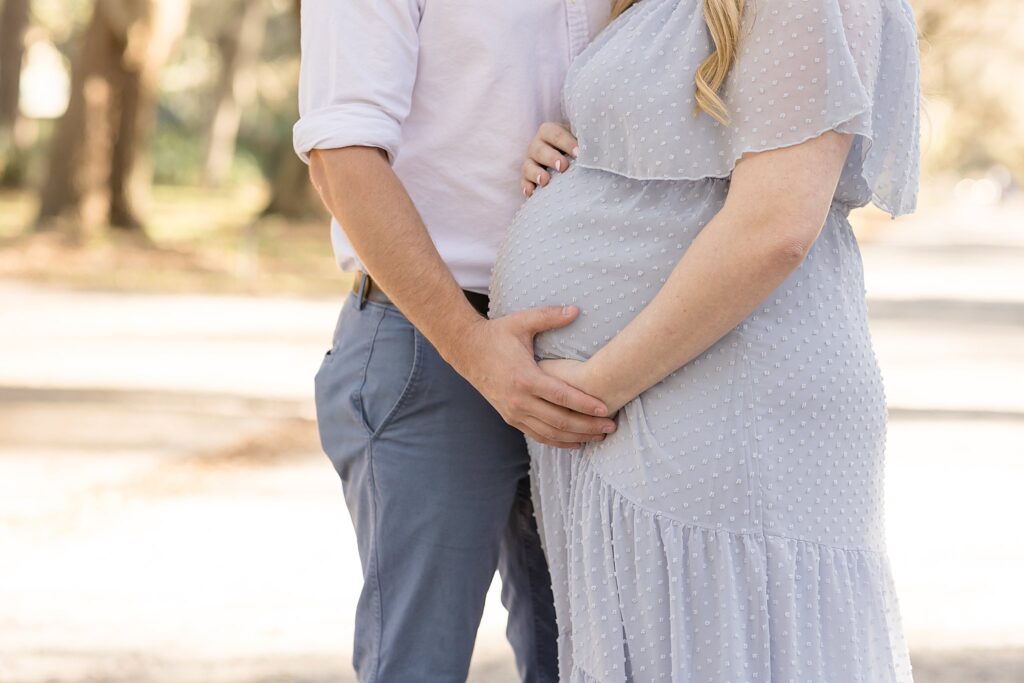 Savannah maternity session focuses in on baby belly while soon-to-be first time parents both hold the belly wearing coordinating outfits of white and grey.