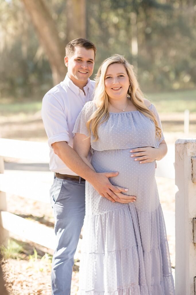 Savannah maternity session is captured by Wisp + Willow Photography Co. at Wormsloe Historic Site of soon-to-be parents both smiling at the camera and holding the baby belly!