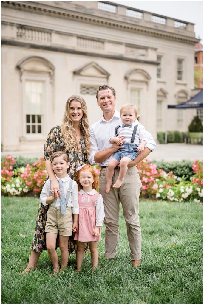 Family of 5 stand and smile at the camera during their Richmond mini session at the VMFA wearing a mix of neutral florals, pink, blue, and white for their coordinating outfits.