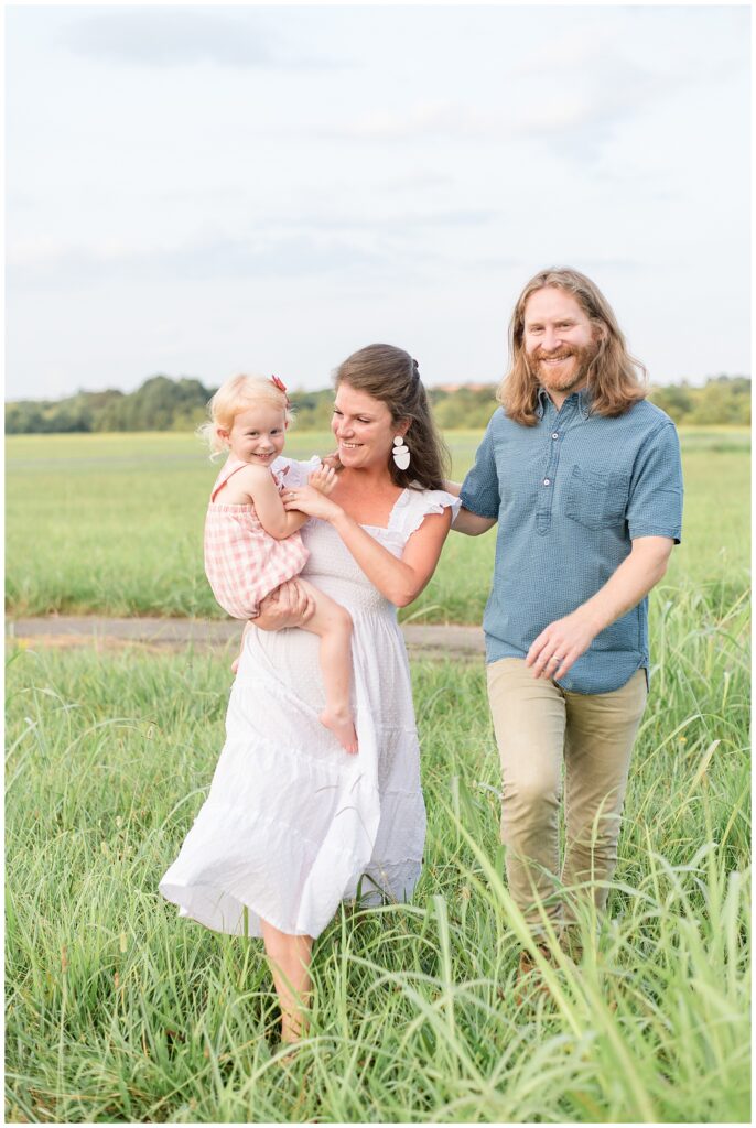 Family of 3 which little girl walk through the grass at Cornelia Fort Airpark in TN for their Nashville family session with Wisp + Willow Photography Co.