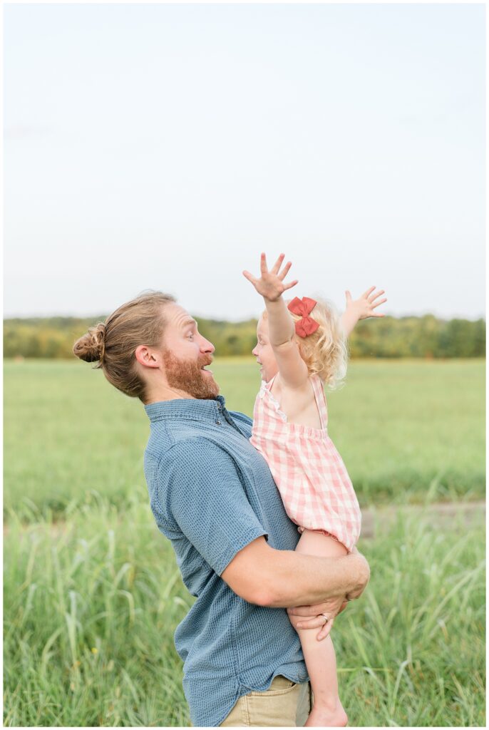 Dad holds daughter as she puts her arms up in the air and they look at each other with surprised happy faces during their family session in Nashville, TN.