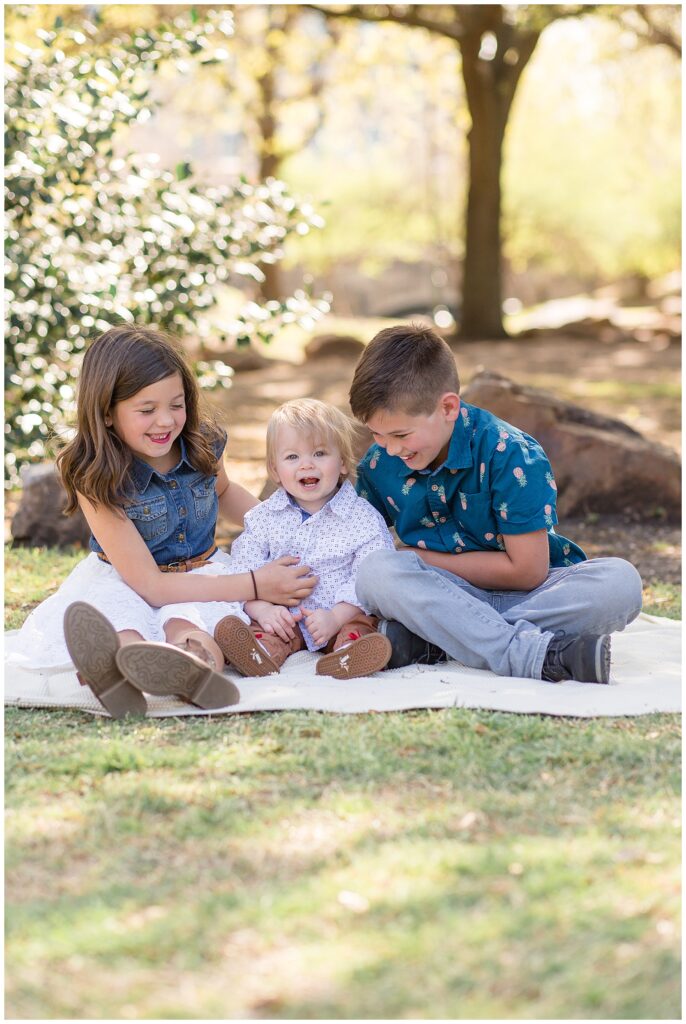 Brother and sister tickle their younger brother during their Frisco family session as they sit on a blank at Frisco Central Park.