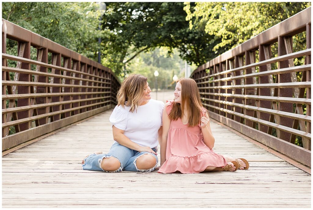 Mom and oldest daughter sit on the bridge at Pinkerton Park in Franklin, TN looking at each other and sharing a mom and daughter moment.