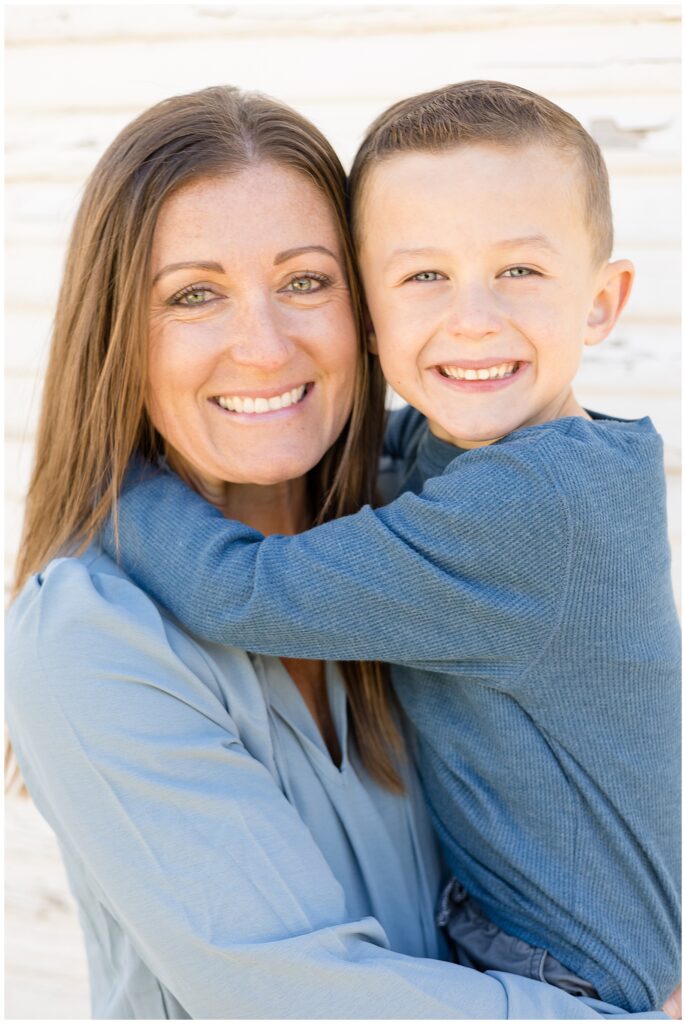 Mom and son go cheek to cheek as they wear muted blues and smile at the camera during their Texas family portrait session.