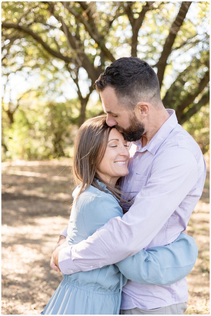 Couple takes a minute to share a hug and husband kisses his wife on her forehead during their Texas family portraits.