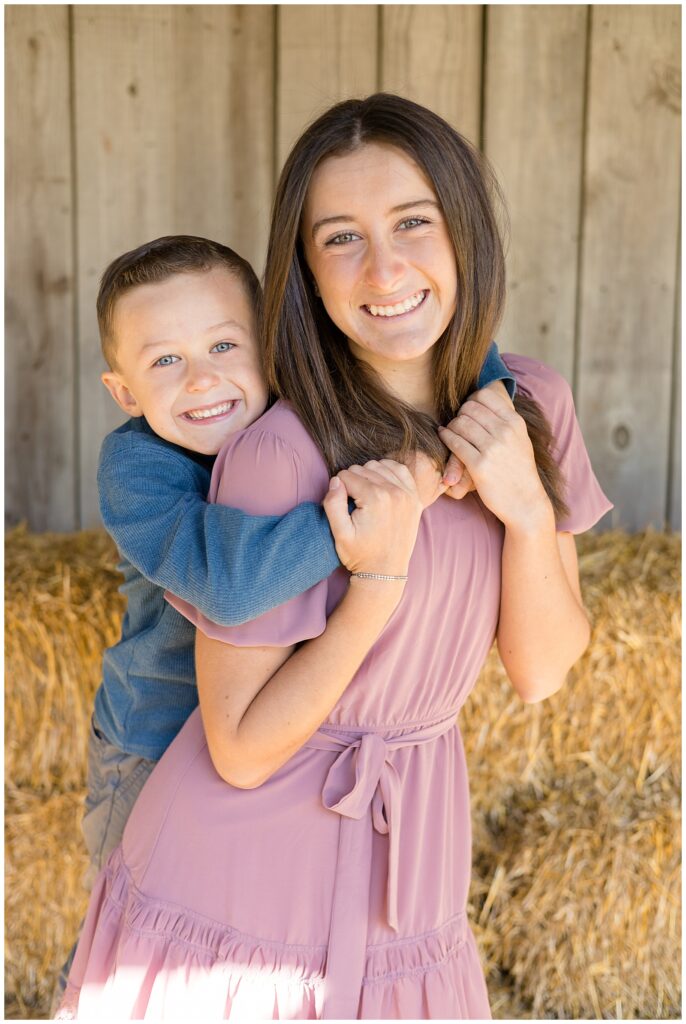 Older sister holds little brother who hugs her from the back and they smile at the camera of Wisp + Willow Photography Co.  Check out more on the blog!