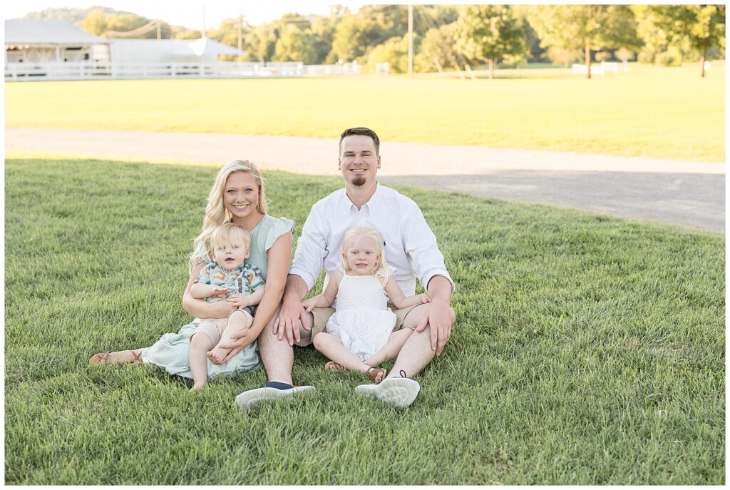 Family of 4 sit in the grass at Harlinsdale Farm in Franklin, TN as Mom and Dad sit with their young son and daughter.  They coordinate in white and mint green colors.