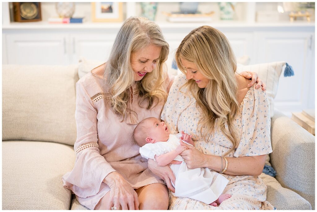 New baby girl is being held in the lap of her mom as new grandma sits next to them and they look down at the new addition to the family.  They coordinate in blush, white, and cream and lace texture on their dresses.