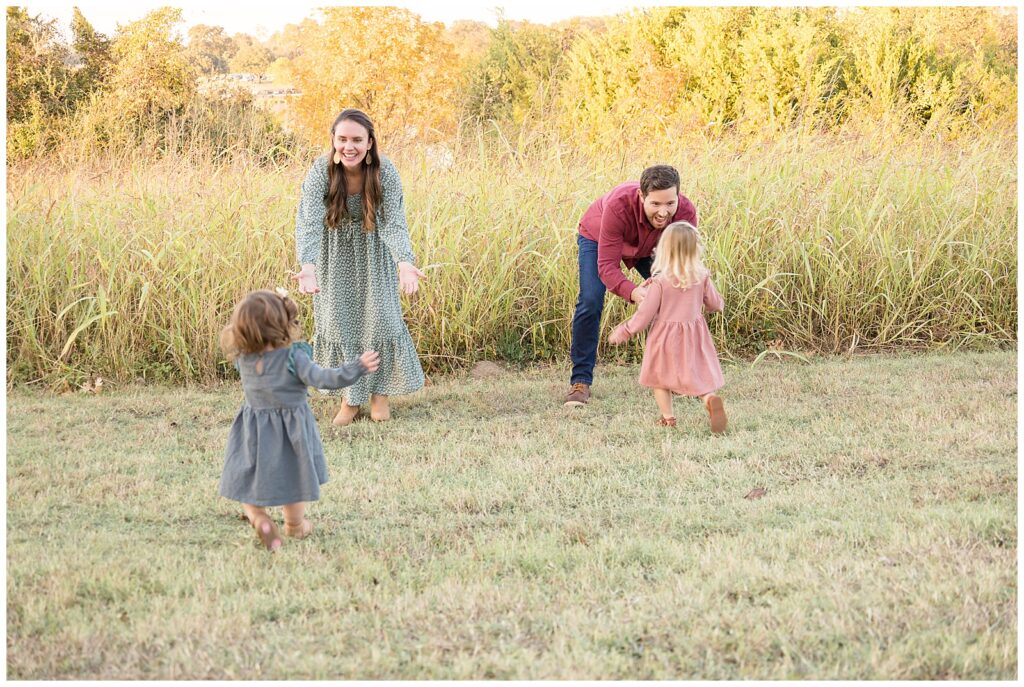 Two little girls run to their Mom and Dad as they prepare to catch them in their arms in a field in Dallas, TX during their Dallas portrait session.