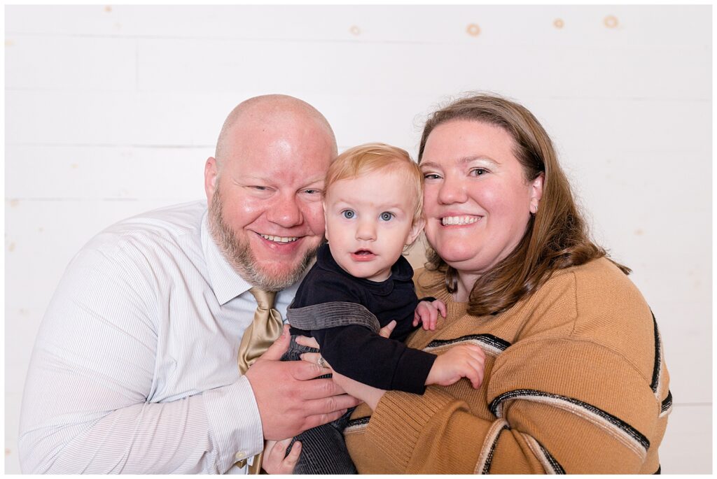 Mom and Dad hold their toddler son in between them as they go cheek to cheek and smile at the camera of Wisp + Willow Photography Co.