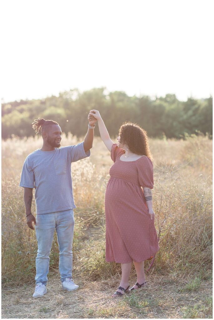 Maternity session at Arbor Hills Nature Preserve has couple dancing together as the husband twirls his wife as they continue to look at each other.  