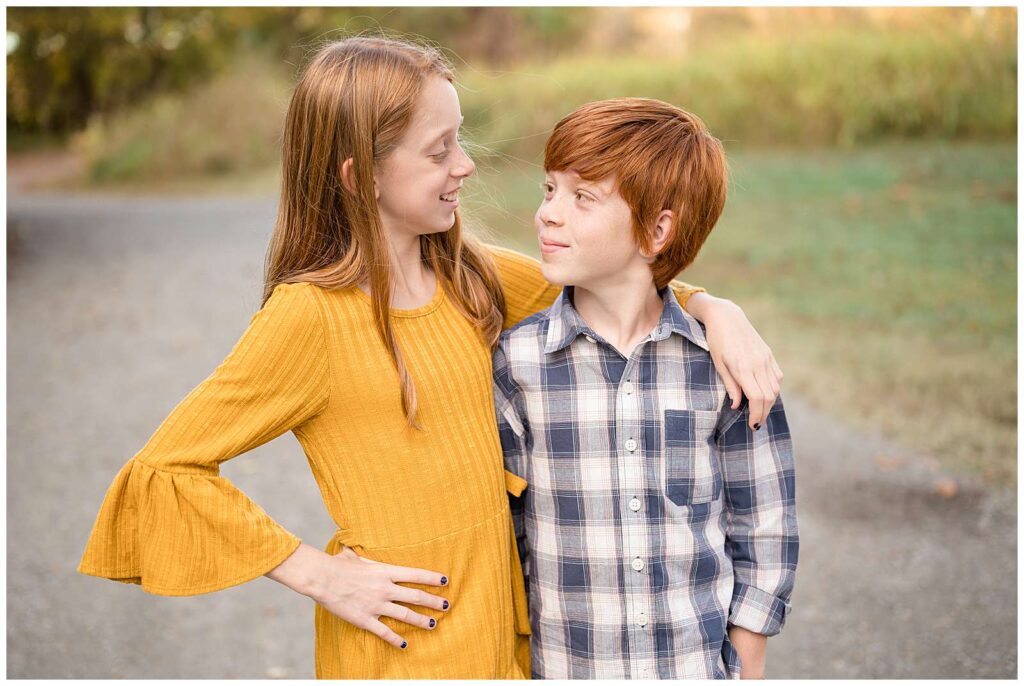 Two red-headed siblings, an older sister and brother, look at each other and smile during their family portrait session in Richmond, VA.