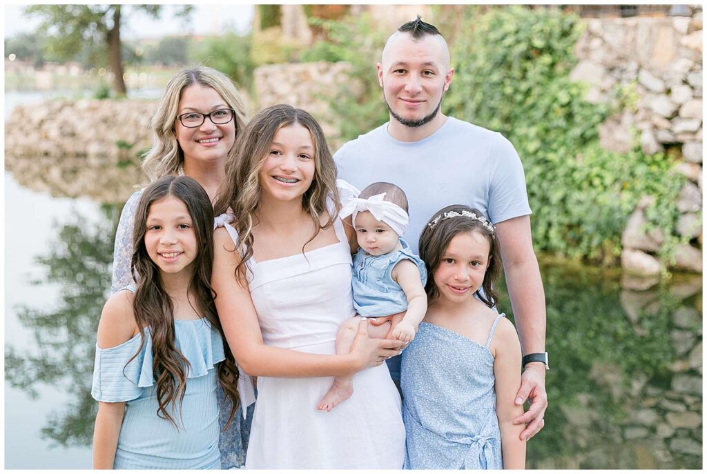 Family of 6 with 4 girls, wear coordinating outfits in light blue and smile at the camera for a new family portrait at Adriatica Village in McKinney, TX.  Click to see more of this family on the blog!